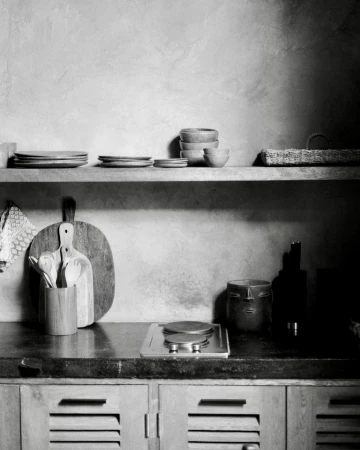 Rustic kitchen interior in monochrome featuring wooden shelves, tableware, cooking utensils, and textured wall, creating a natural ambiance.