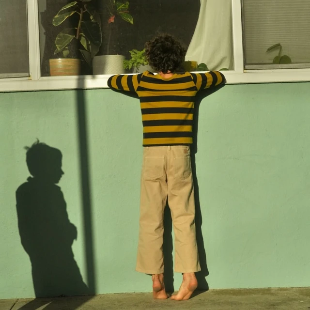 Back view of child standing on tiptoes, looking out a window of a mint-green building with an interior houseplant on display.