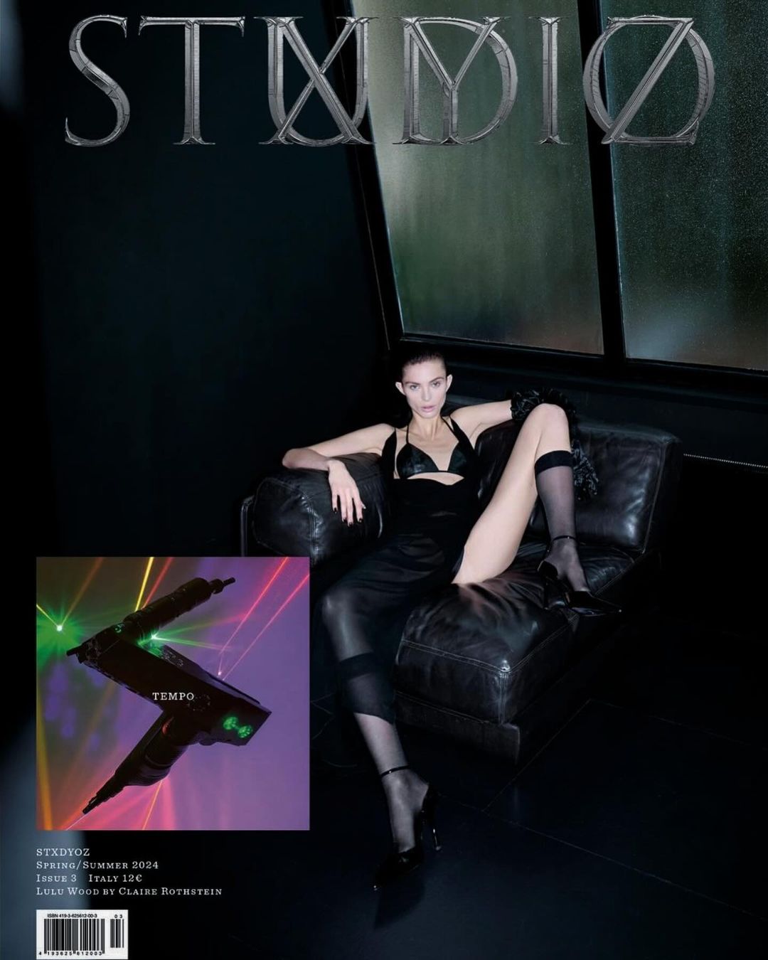Magazine cover featuring a woman in a black outfit reclining on a black leather chair against a dark gray backdrop with visible text.