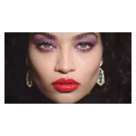 Close-up of a woman's face with vibrant purple eyeshadow and glossy red lipstick against a dark background, showcasing beauty and makeup.