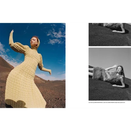 A woman in a light yellow dress with long sleeves and a head covering poses in an open desert landscape under a blue sky.