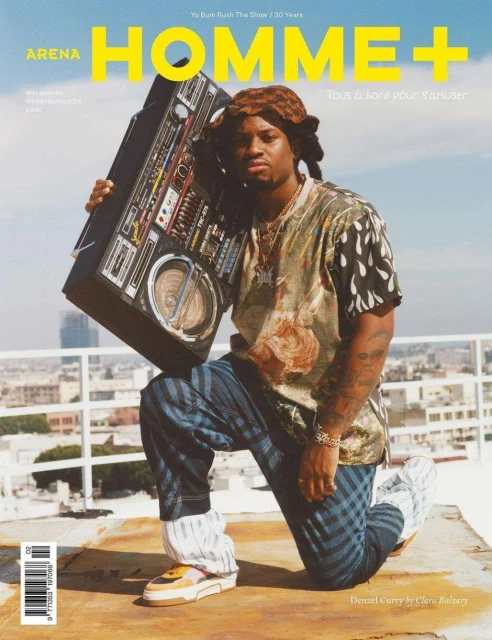 Arena Homme+ magazine cover featuring musician Denzel Curry kneeling on a rooftop, holding a boombox, wearing a patterned shirt and jeans.