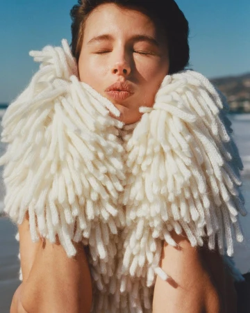 Portrait of a woman wearing a textured white fringe sweater with her eyes closed against an outdoor coastal background