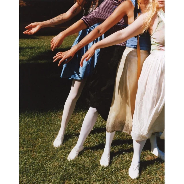Group of women in vintage dresses and white tights standing on grass. Sunny day. Fashion photography in an outdoor setting.