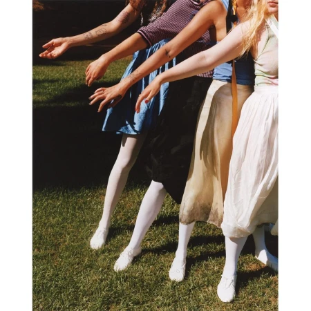Group of women in vintage dresses and white tights standing on grass. Sunny day. Fashion photography in an outdoor setting.