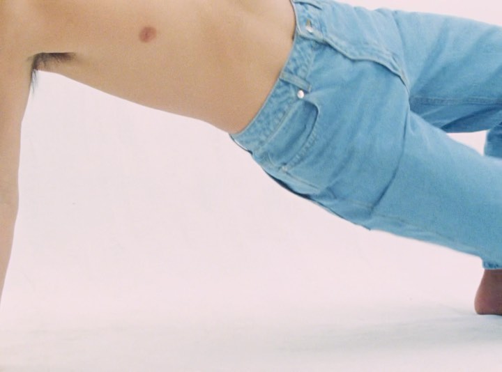 Close-up portrait of a shirtless person wearing light blue denim jeans against a plain white studio background.