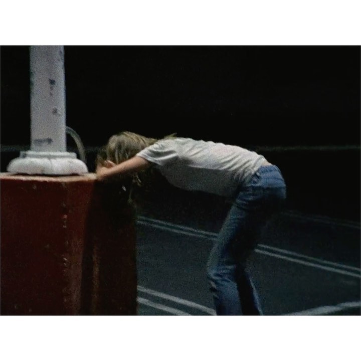 Young woman in blue jeans leaning on a vintage-style water fountain on a road. Dark, nighttime setting with roadside lines.