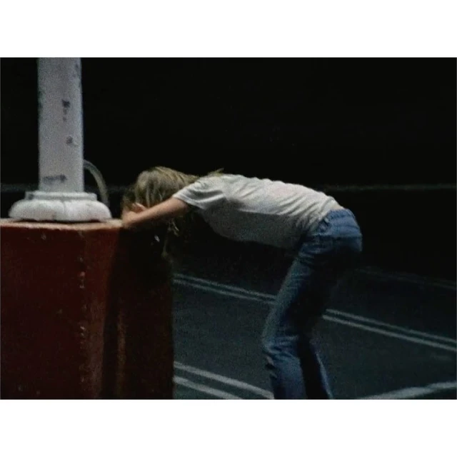 Young woman in blue jeans leaning on a vintage-style water fountain on a road. Dark, nighttime setting with roadside lines.