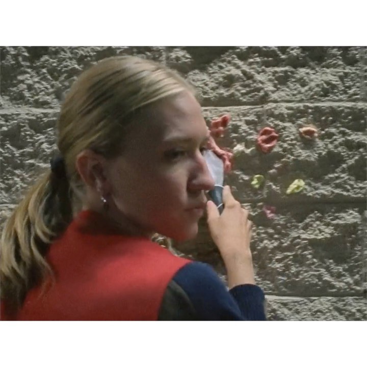 Adult female applying white cream to her face while standing in front of textured wall with various rock climbing holds.