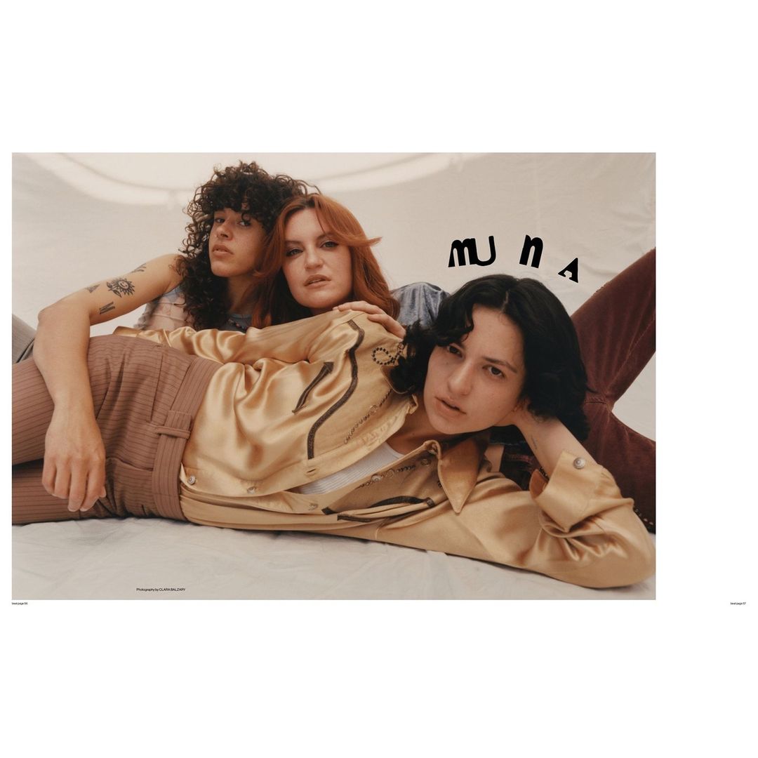 Three adult women are lying down closely together in a studio setting, with neutral tones and soft lighting, for a fashion editorial.