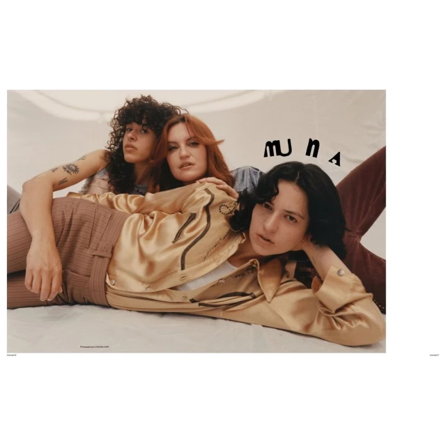 Three adult women are lying down closely together in a studio setting, with neutral tones and soft lighting, for a fashion editorial.