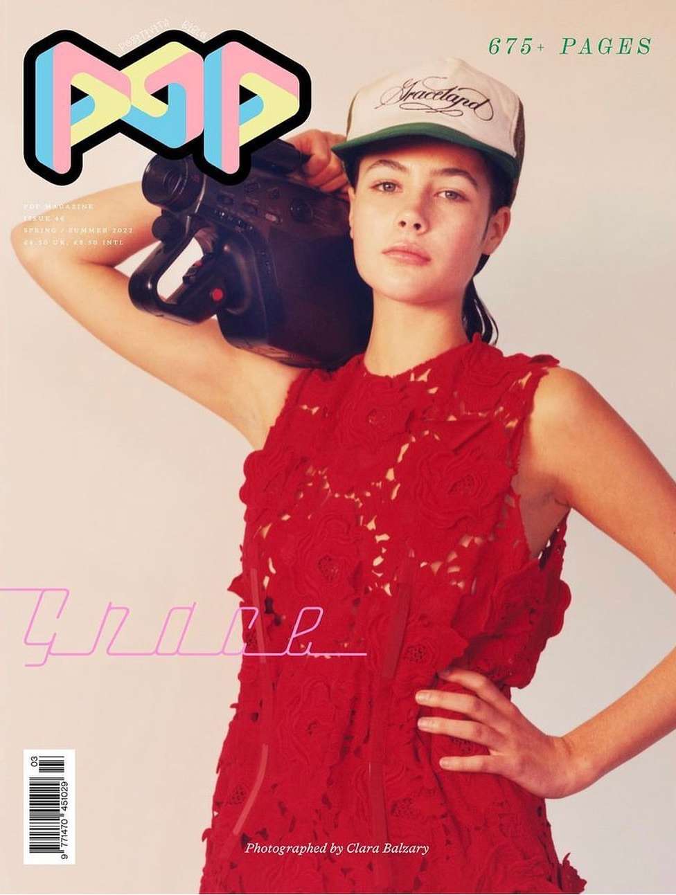 Magazine cover featuring woman in red dress and trucker hat, holding a vintage video camera against a peach backdrop.