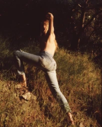 Woman wearing denim jeans posing outdoors among tall grass in warm lighting by photographer Clara Balzary