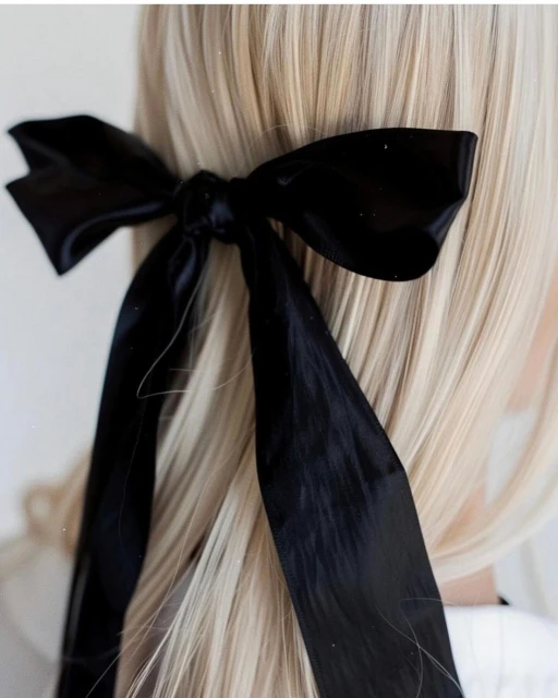 Close-up of blond hair styled with a large black ribbon bow, showcasing an elegant and simple hairstyle against a neutral background.