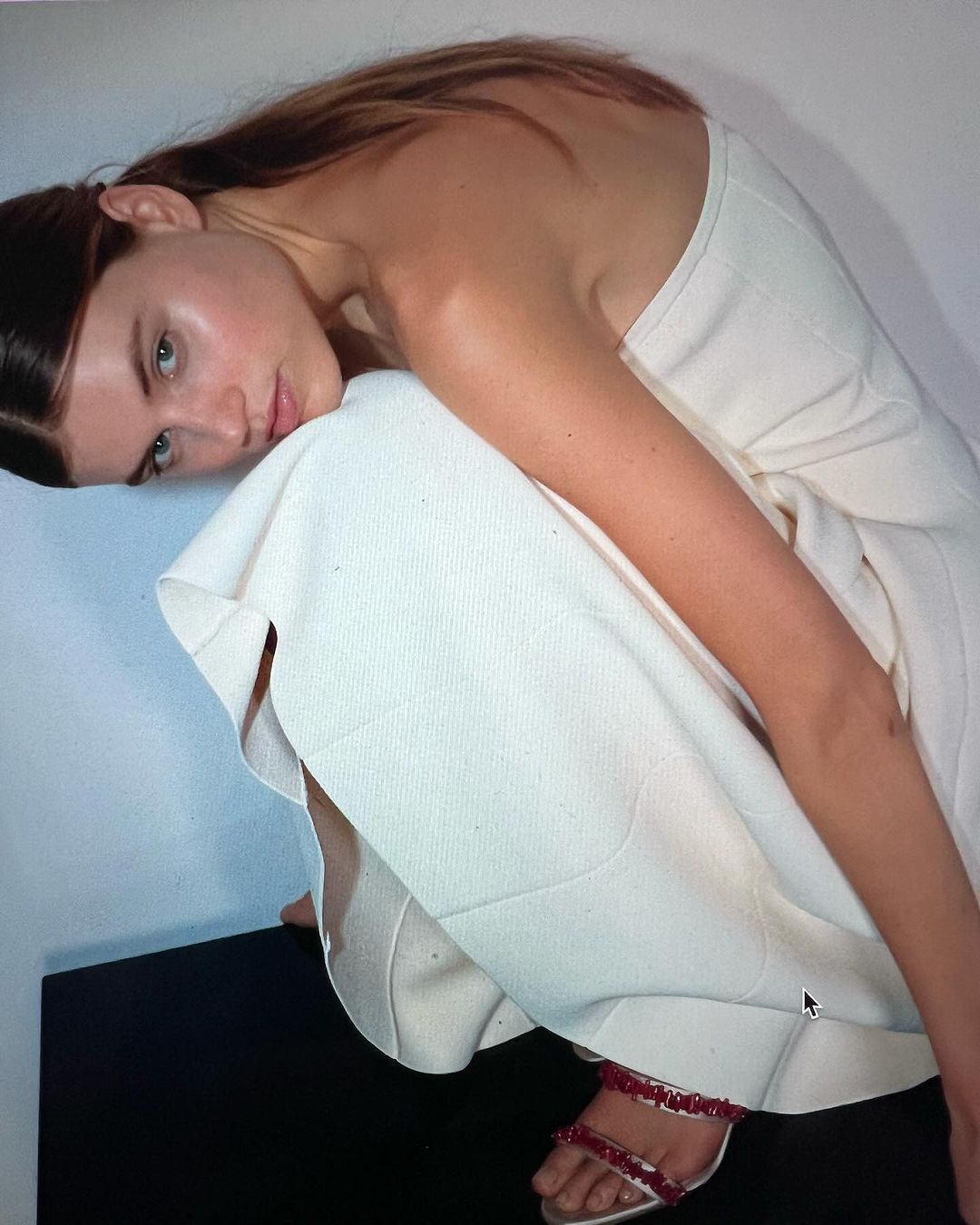 Model in a cream strapless dress crouching against a plain white wall, captured by photographer Claudia Grassl.