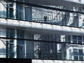 Three men standing on different elevated glass balconies inside a modern multi-story office building atrium
