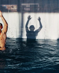 Swimmer partially visible on the left side raising arms next to a dramatic shadow on a pool wall in Paris by Claudia Imbert