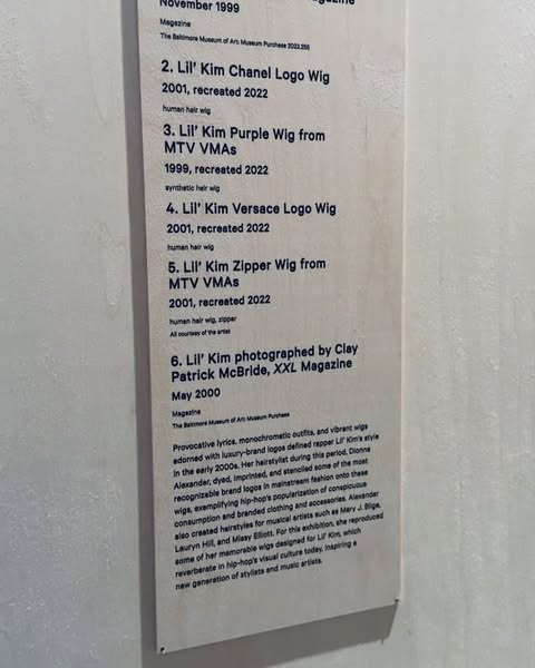 A display featuring information about Lil' Kim's wigs. The display is indoors and features a description of the wigs.