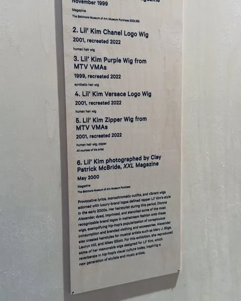 A display featuring information about Lil' Kim's wigs. The display is indoors and features a description of the wigs.