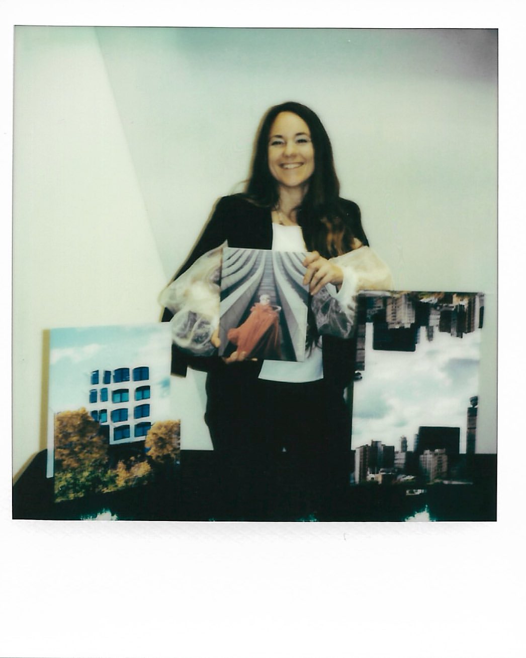 Smiling woman holding an art photograph indoors with two additional art photographs displayed on a table, creating a vibrant scene.