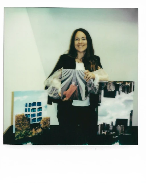 Smiling woman holding an art photograph indoors with two additional art photographs displayed on a table, creating a vibrant scene.