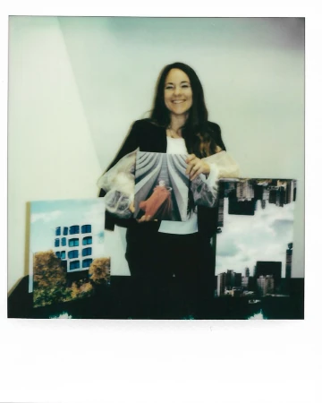 Smiling woman holding an art photograph indoors with two additional art photographs displayed on a table, creating a vibrant scene.