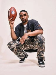 Man crouching while holding up a football against a plain light background, photographed by Clay Patrick Mcbride.