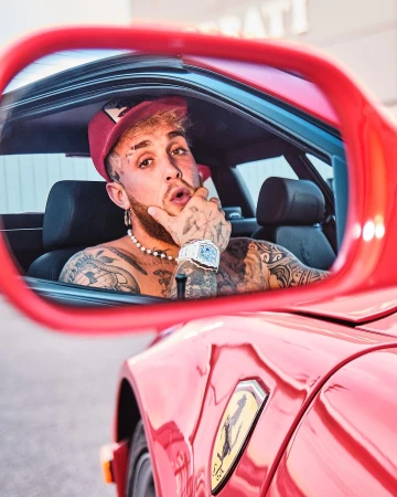 Man with tattoos sitting inside a red car viewed through the side mirror, photographed by Clay Patrick Mcbride