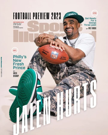 Jalen Hurts sitting on floor holding an NFL football wearing camouflage overalls green cap and sneakers, photographed by Clay Patrick Mcbride.