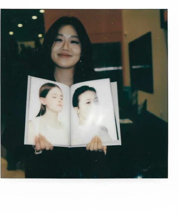 Woman holding open a photography book featuring two portraits, captured on Polaroid film by Clay Patrick Mcbride