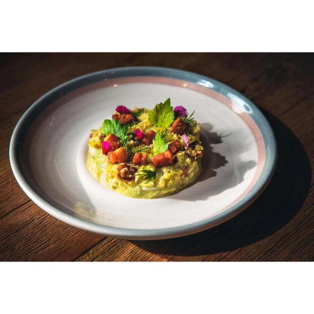 Gourmet salad featuring fresh herbs, edible flowers, and diced meat served on a white plate, set against a dark wooden surface.