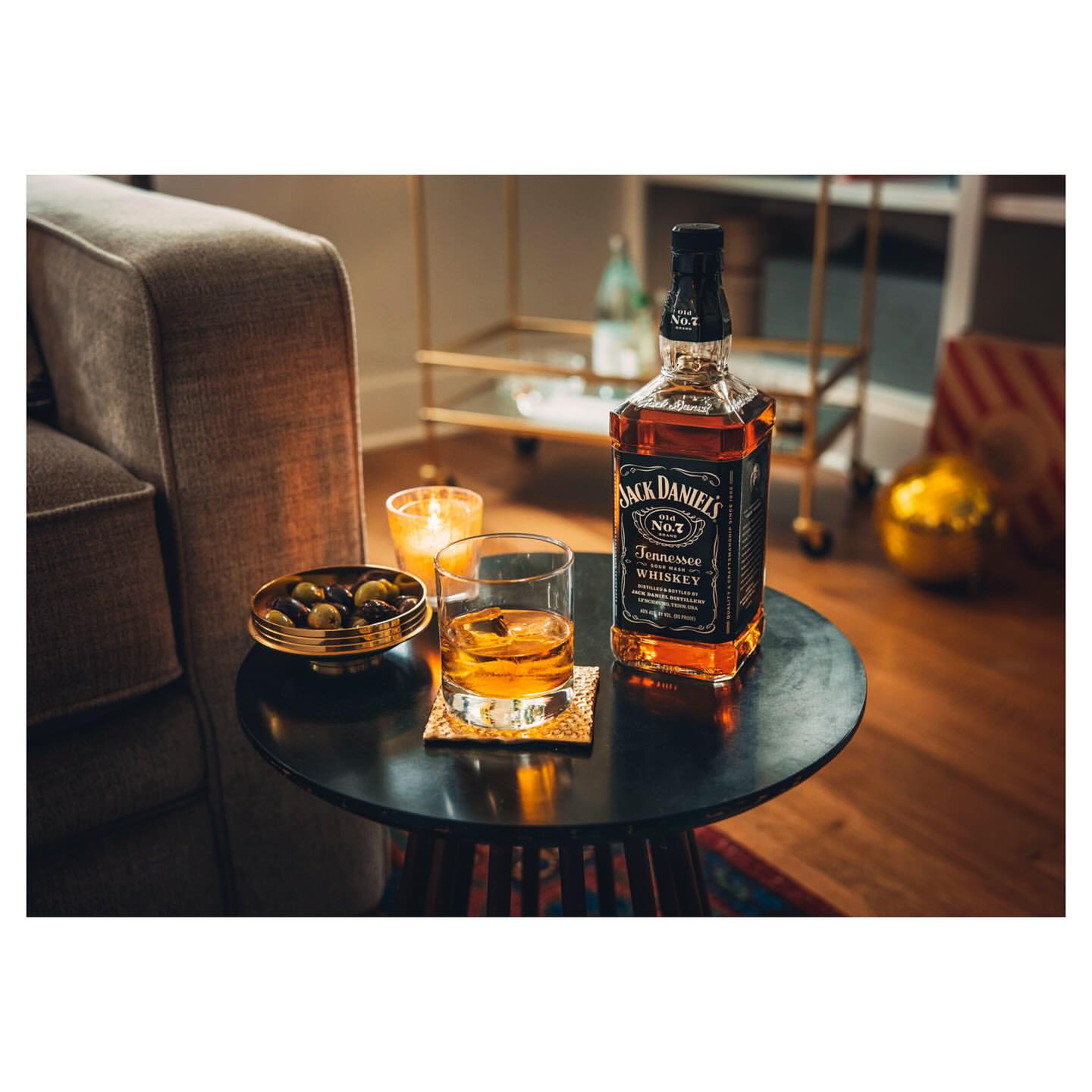 Bottle of Jack Daniel's Tennessee Whiskey, a glass of whiskey, olives, and a candle sit on a round, black table.