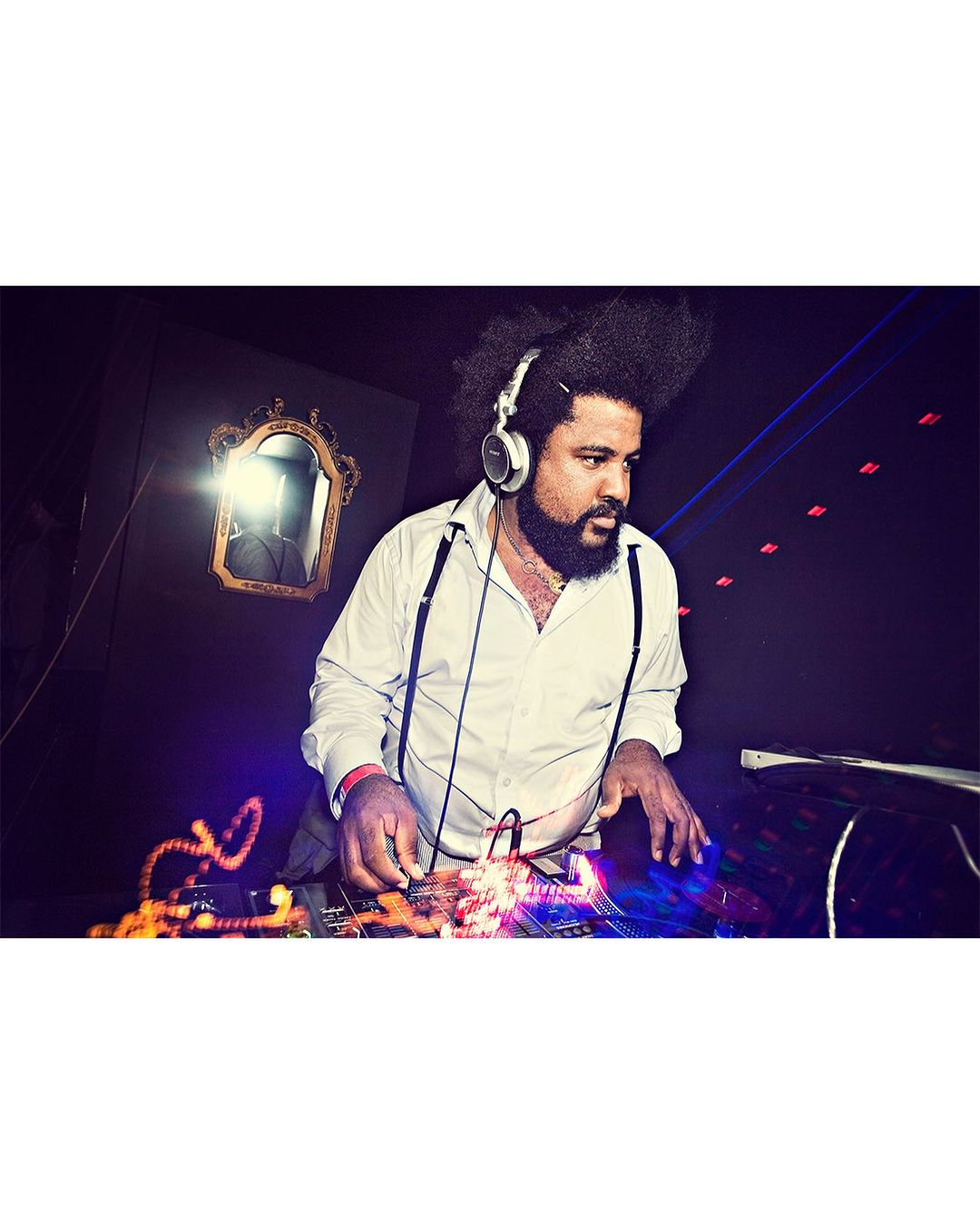 Man with headphones DJing at a club with stage lights and a vintage mirror, creating a vibrant atmosphere with dynamic lighting effects.