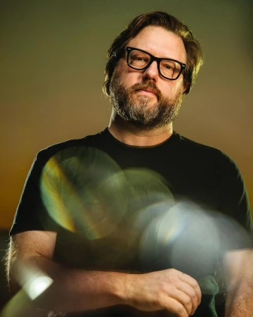 Portrait of a bearded man wearing thick black frame glasses and a black t shirt photographed by Clayton Hauck.