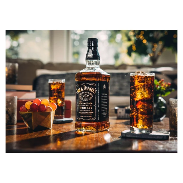 Bottle of Jack Daniel's whiskey with ice-filled glasses on a wood table, with a couch and Christmas lights softly blurred in the background.