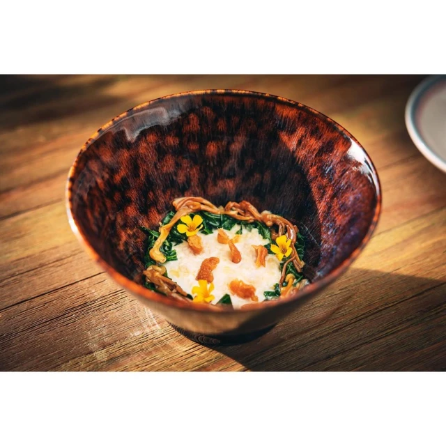 Close-up of a beautifully plated food dish featuring white cream and edible yellow flowers in a decorative brown ceramic bowl on a table.
