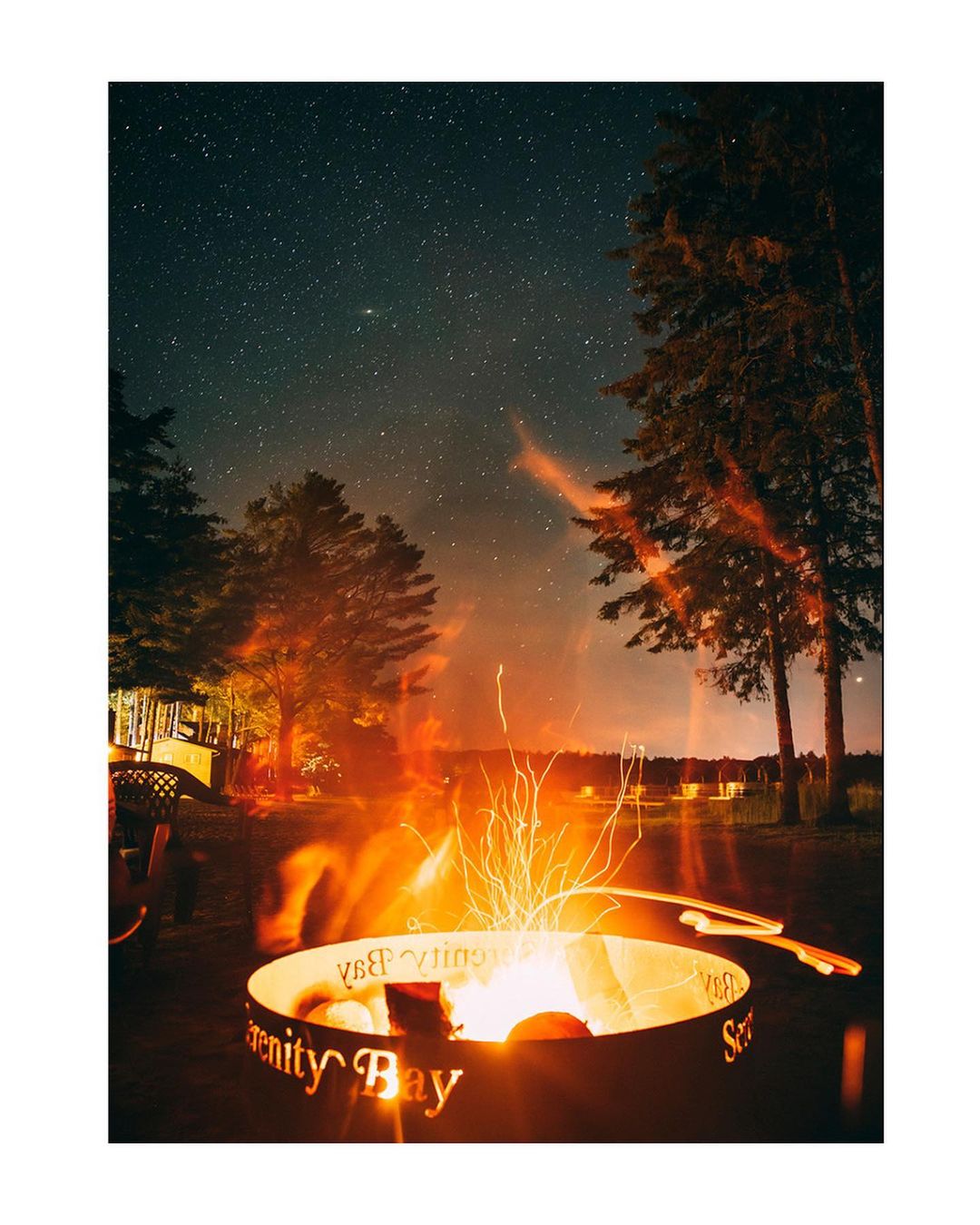 Nighttime view of a burning fire pit with cut-out text, set amongst trees under a starry sky, creating a warm and inviting outdoor ambiance.