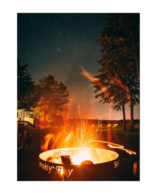 Nighttime view of a burning fire pit with cut-out text, set amongst trees under a starry sky, creating a warm and inviting outdoor ambiance.