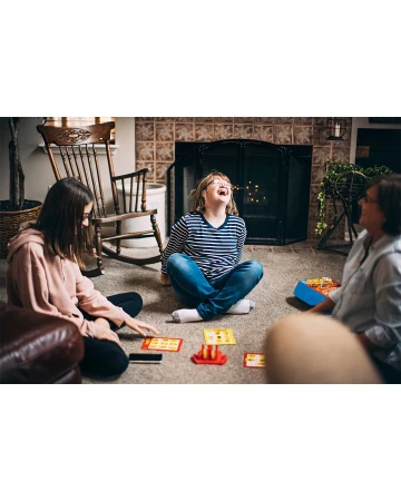 Three people play a board game on the floor of a living room near a fireplace, creating a cozy and engaging family activity indoors.