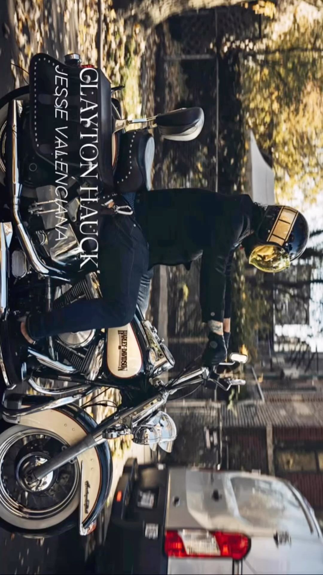 Man wearing a helmet riding a motorcycle on a street near buildings, with cars visible in the background on an overcast day.
