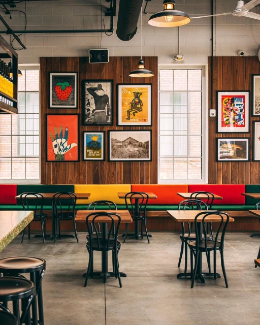 Restaurant interior with colorful booth seating, wooden tables and black chairs, and framed art on a wood-paneled wall.