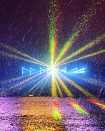 Snowy outdoor scene with vibrant laser light display illuminating the field and falling snow, creating a dynamic and colorful visual.
