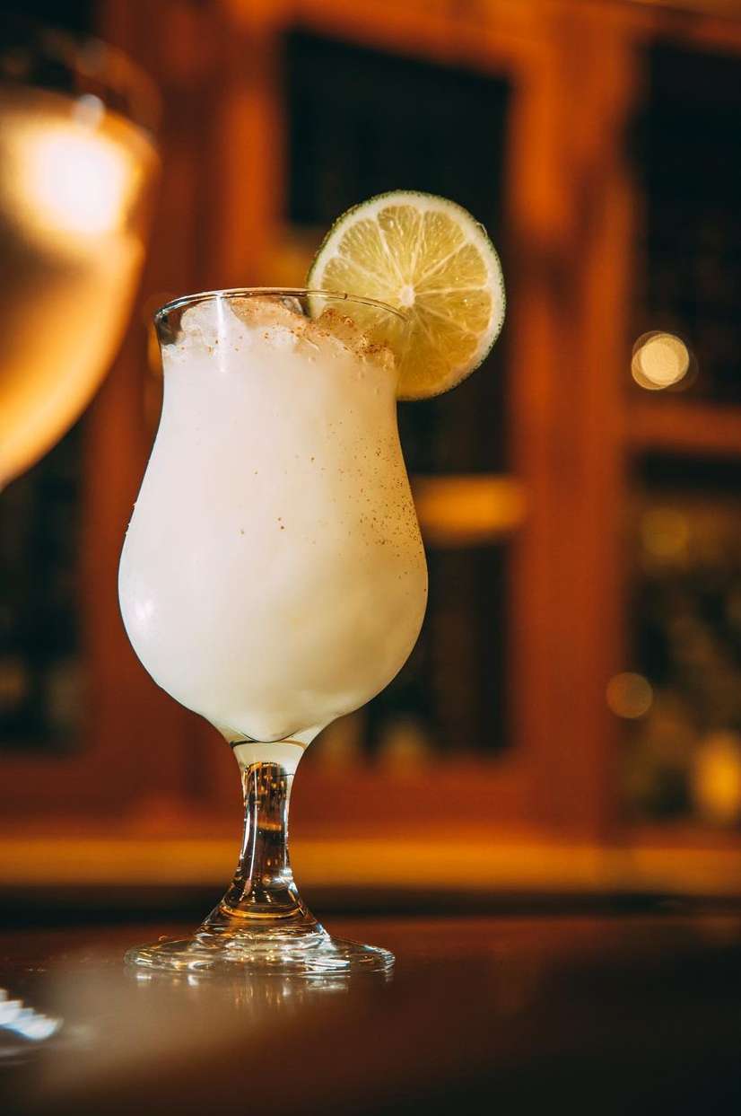 Cocktail glass filled with a white drink and garnished with a lime slice on a wooden surface against a blurred backdrop.