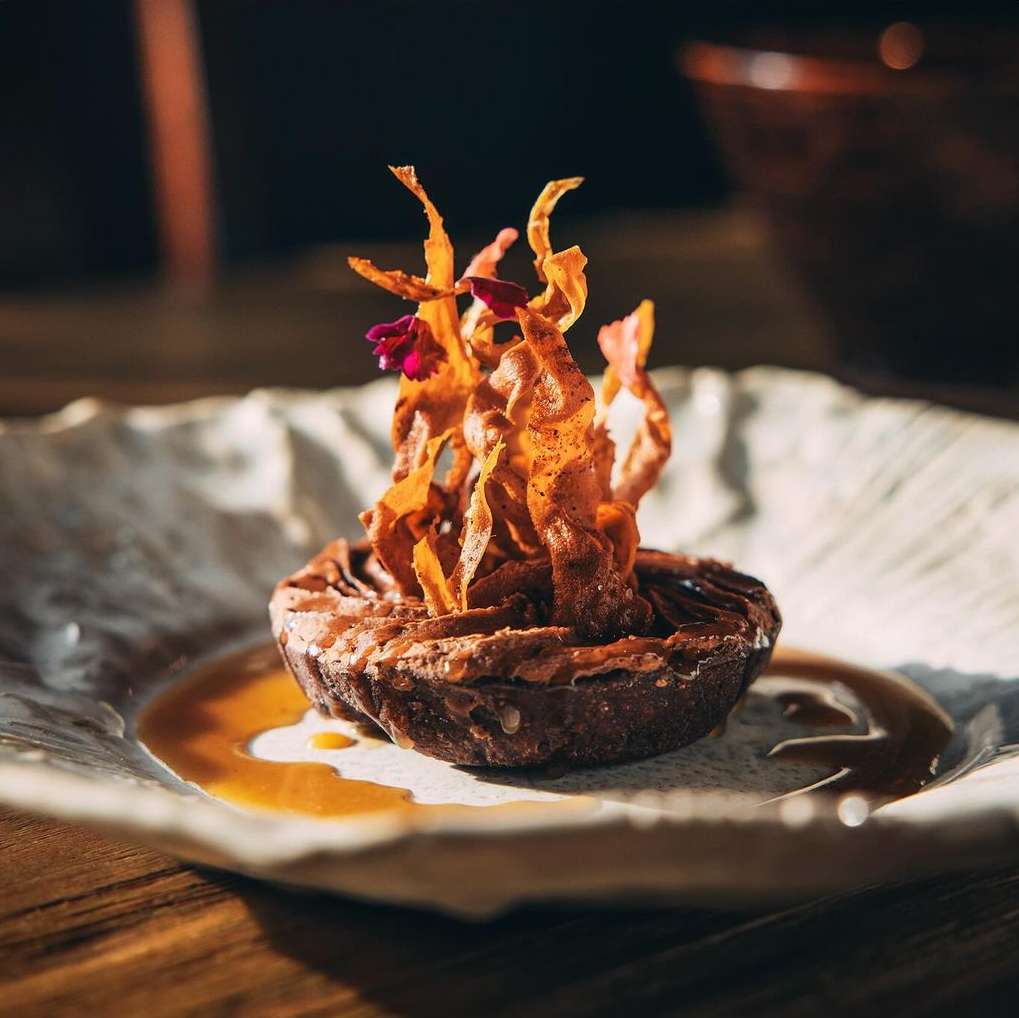 Chocolate dessert with crunchy topping served on decorative plate, in warm lighting. Food photography for restaurant menu or advertising.
