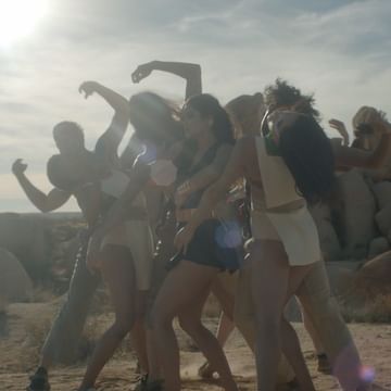 A group of six people dance together in a desert landscape under a bright sky, exhibiting dynamic poses and expressive movement.