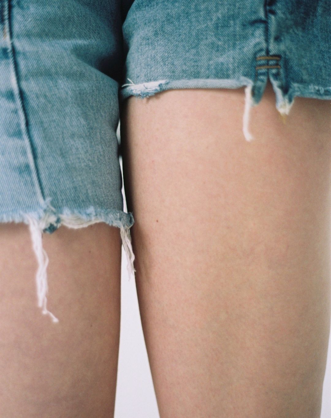 Close-up shot featuring a fair-skinned adult human wearing denim shorts, against a neutral backdrop for fashion or beauty content.