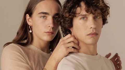 Two adults posing in a studio setting, wearing neutral-toned shirts and minimal jewelry, with soft lighting and a focus on facial features.