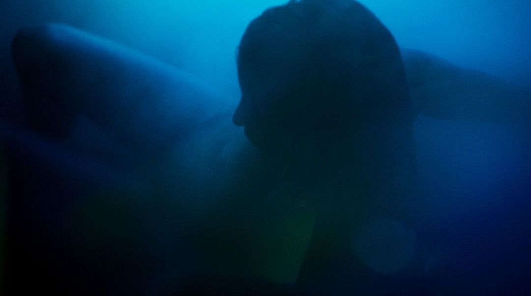 Silhouette of person underwater in a dark blue setting, abstract and atmospheric.