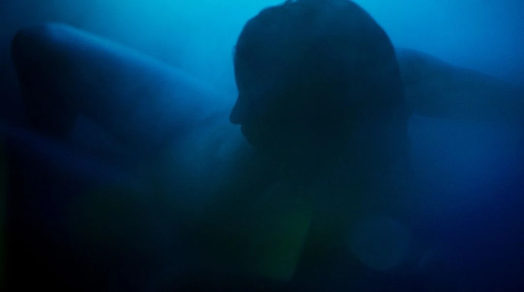 Silhouette of person underwater in a dark blue setting, abstract and atmospheric.