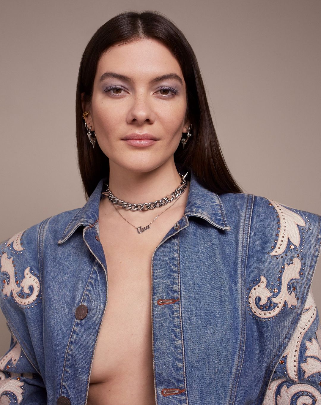 Portrait of a brunette woman wearing a denim jacket and silver necklaces, showcasing fashion and personal style in a studio setting.